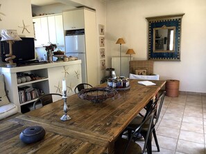 A dining area with a wooden table, chairs, a television, kitchen cabinets, and decorative items.