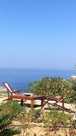 En uppsättning bestående av en träfåtölj och ett bord, placerad på en terrass med utsikt över en vattenyta.