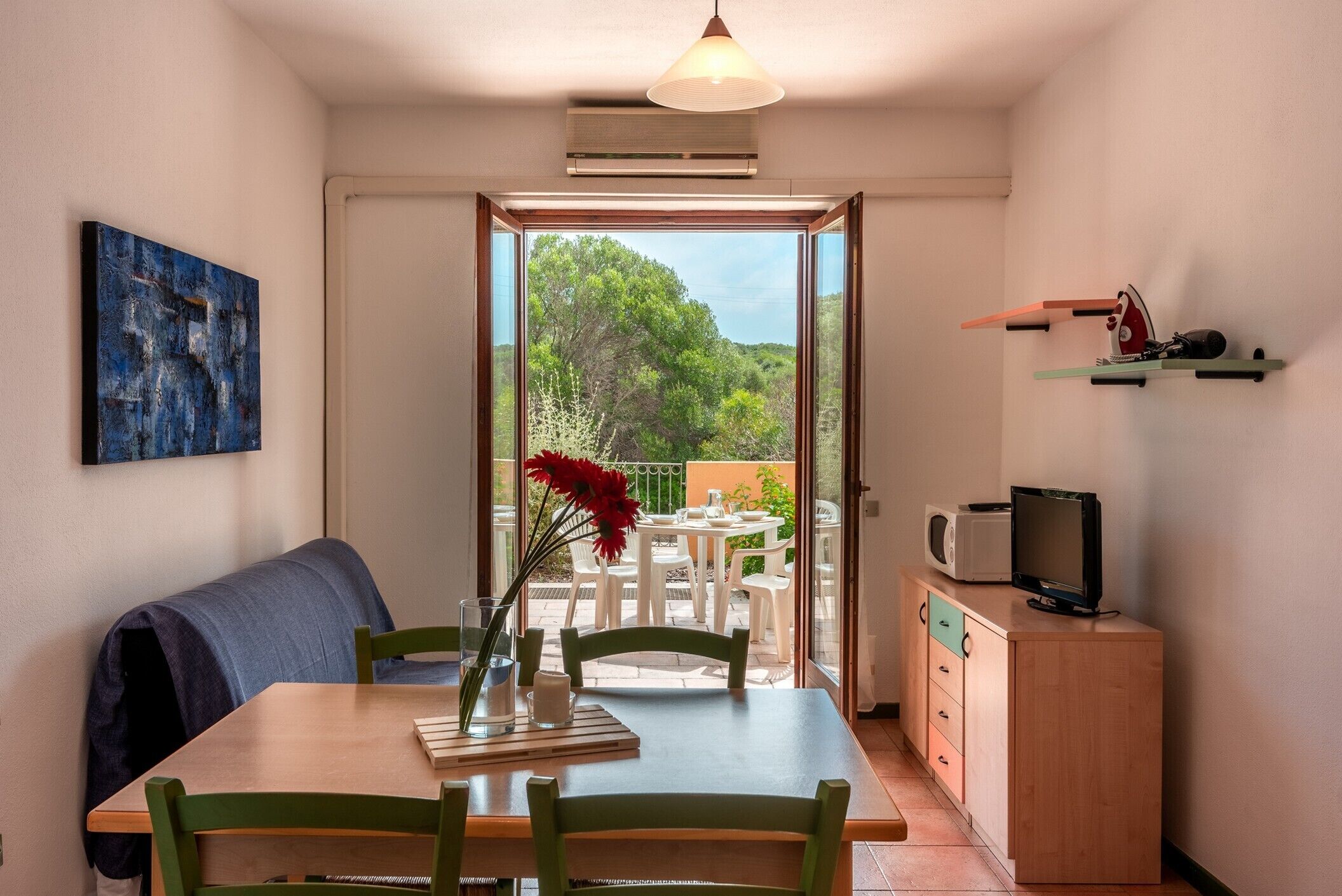 Un área de comedor con una mesa, sillas, un banco, un televisor en un mueble y un cuadro en la pared.
