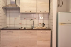 Ett kök med ljusa träskåp, en diskho i rostfritt stål och ett vitt kylskåp.