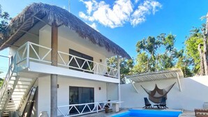 A two-story building with a thatched roof, a balcony, and a pool area with lounge chairs. - Small Hidden Spot In La Veleta (Tulum)