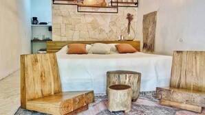 A bedroom with a stone wall, a bed with white bedding, and wooden furniture. - Small Hidden Spot In La Veleta (Tulum)
