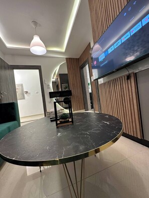 A modern living room with a round black marble table, a mounted TV displaying streaming services, and a ceiling light fixture. - JRE Modern Apartment In Abdoun-amman (Amman)