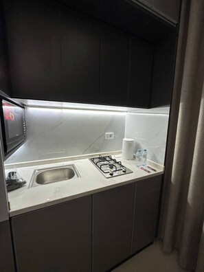 A compact kitchen with a gas stove, a microwave, a sink, and a countertop. - JRE Modern Apartment In Abdoun-amman (Amman)