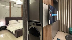 Camera d'albergo moderna con lavatrice e asciugatrice integrate, televisore a schermo piatto, un letto e una piccola zona pranzo.