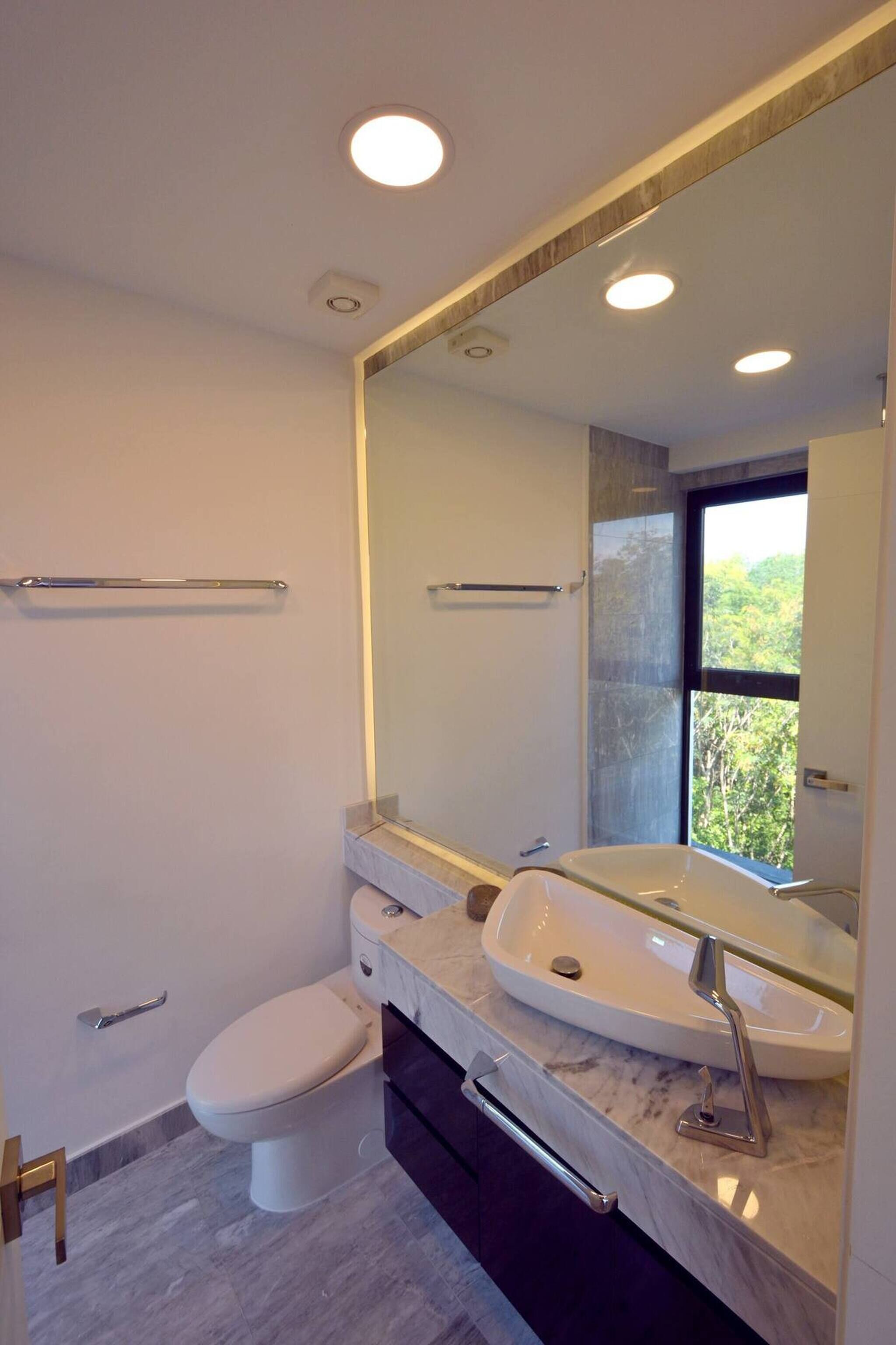 A modern bathroom with a white toilet, a large mirror, and a marble sink.
