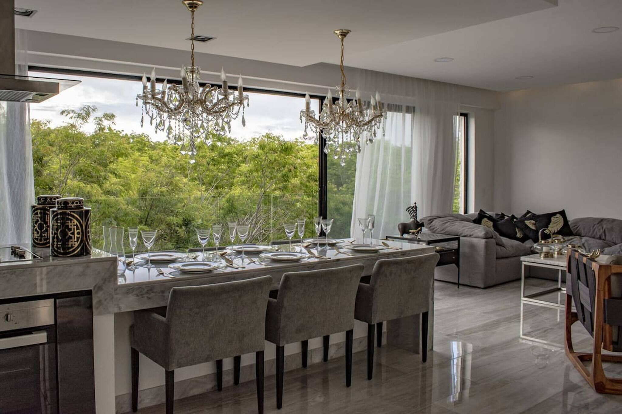 Un comedor moderno con una mesa grande dispuesta para seis personas, una araña y vistas de exuberante vegetación.