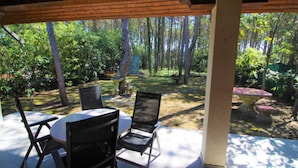 A covered patio with two chairs and a table, overlooking a forested area with trees and a garden. - Spacious Villa With Garden by the sea (Lignano Sabbiadoro)
