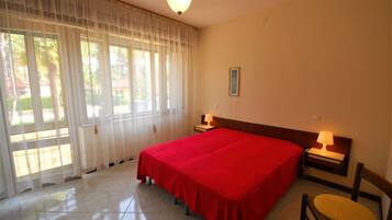 A hotel room with a large bed, two bedside tables with lamps, a chair, and a window with sheer curtains.