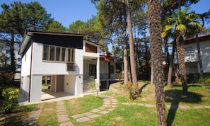 A modern two-story house with a stone pathway leading to the entrance, surrounded by trees and a well-maintained lawn. - Villa Surrounded by Nature Near the sea (Lignano Sabbiadoro)