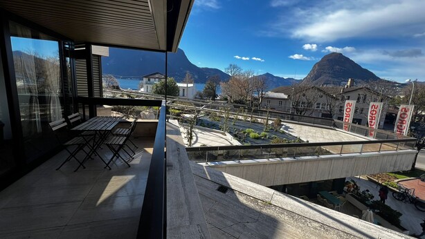 En moderne balkon med udsigt over et bjergrigt landskab og et vandområde.