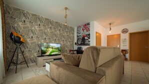 A living room with a television, a sofa, a wall with newspaper print, and a motorcycle poster. - The Queen Apartments - Villa Adriana (Luxembourg City)