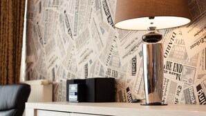 A room with a wooden cabinet, a lamp, and a newspaper-patterned wallpaper. - The Queen Apartments - Villa Adriana (Luxembourg City)