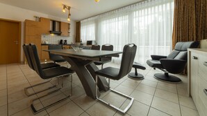 A modern kitchen with a dining area, featuring a table with chairs, a sofa, and a large window with curtains. - The Queen Apartments - Villa Adriana (Luxembourg City)