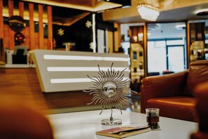 A sun-shaped metal sculpture on a table with a glass of whiskey and a menu. - Midis Otel (Edirne)