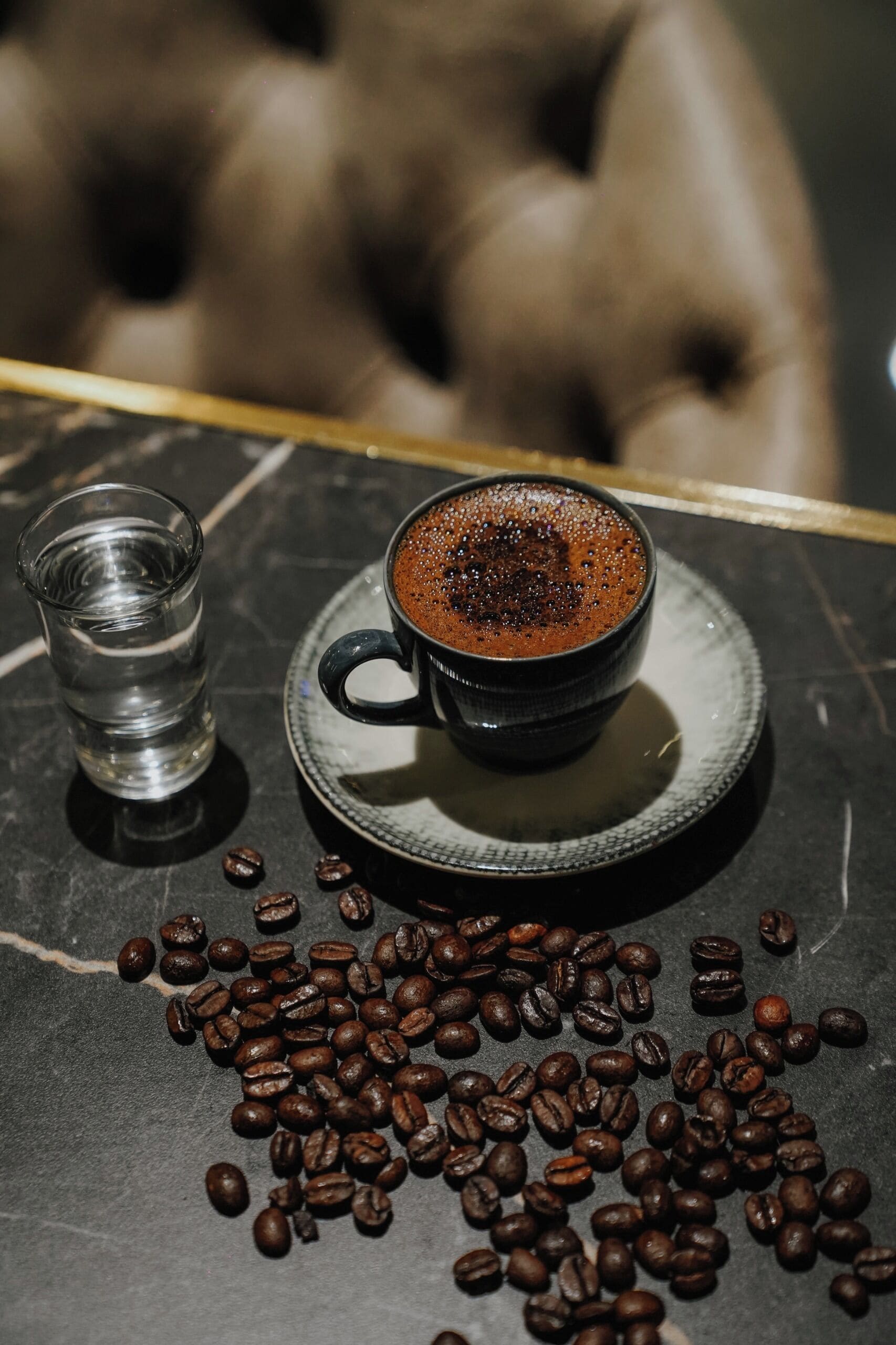 A cup of coffee on a saucer with coffee beans scattered around.