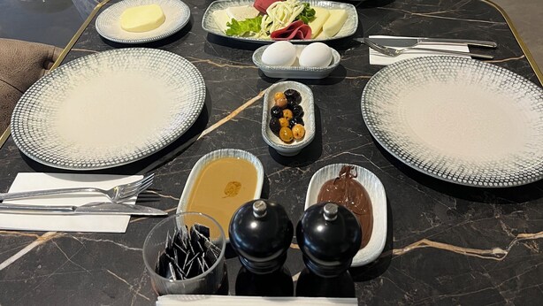 A dining table set with various dishes, including a bowl of olives, a plate of sliced vegetables, and a bowl of soup. - Midis Otel (Edirne)