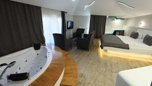 A modern hotel room with a large bathtub, a bed, a desk with a chair, and a television. - Midis Otel (Edirne)