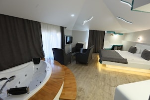 Una habitación de hotel moderna con una bañera grande, una cama, un escritorio con una silla y una televisión.