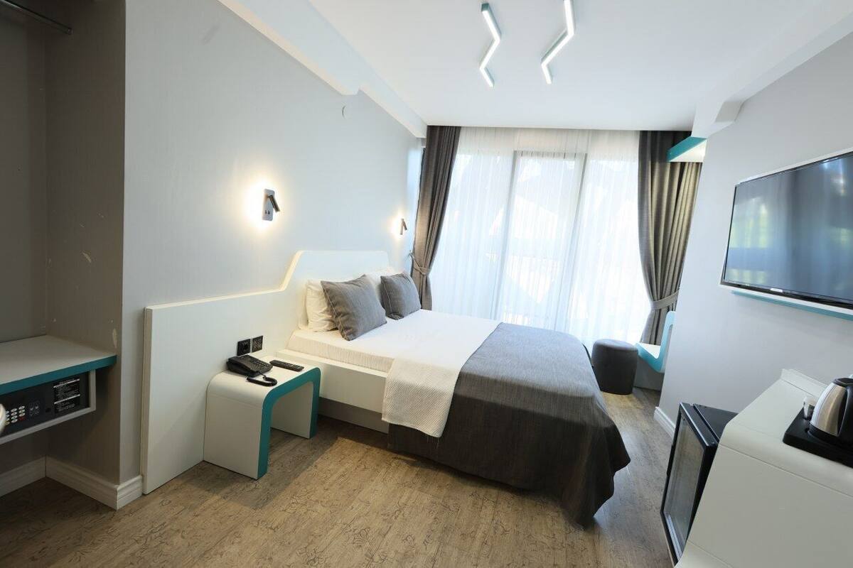 Una camera d'albergo moderna con un letto, un comodino, una televisione e una scrivania con un computer.