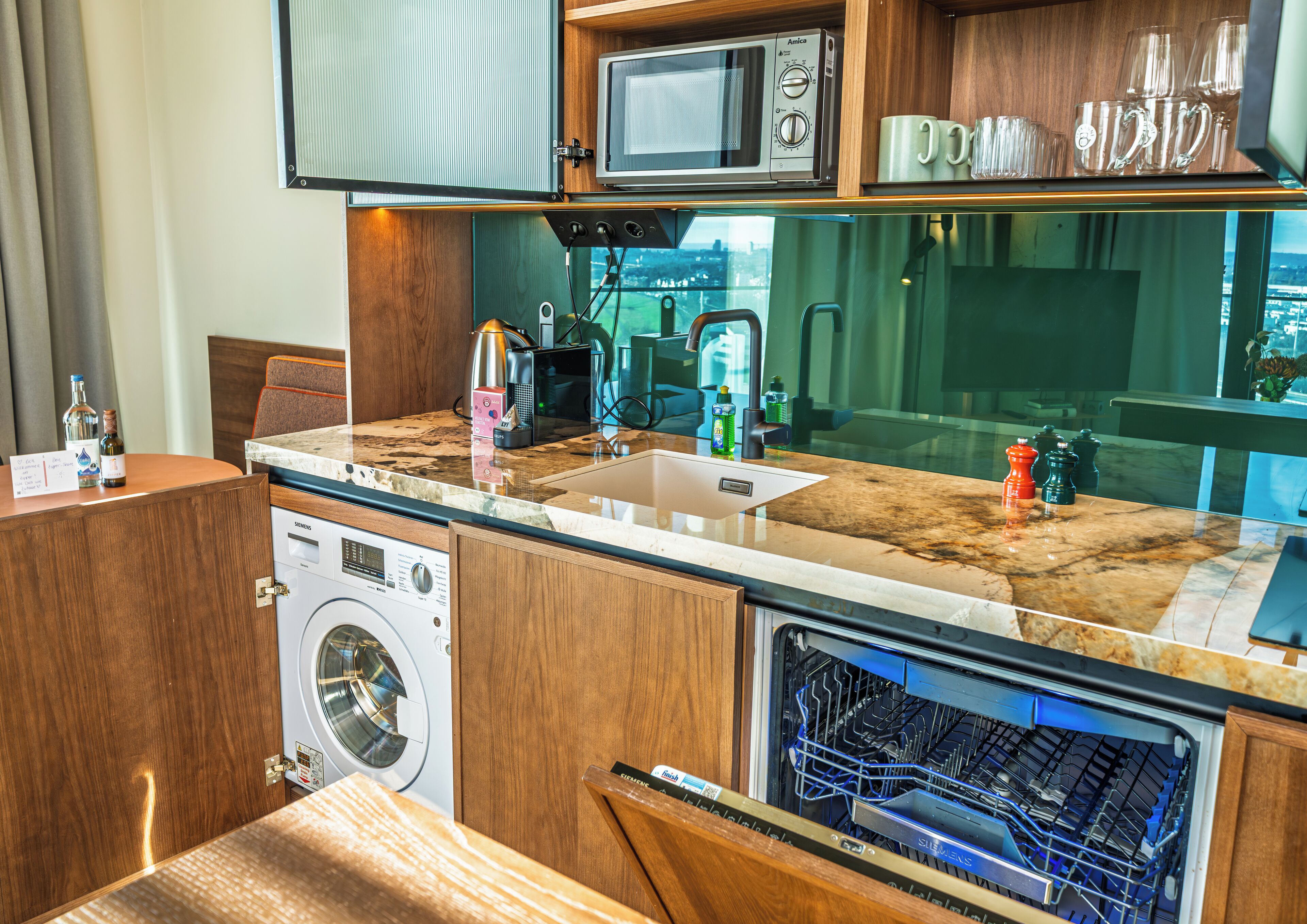 Una cocina compacta con microondas, lavabo y lavavajillas, y vista a la ciudad desde la ventana.