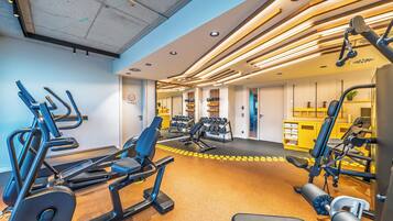 Un gimnasio con equipo de ejercicio, una pared amarilla y una puerta con la leyenda 'Wellness'.