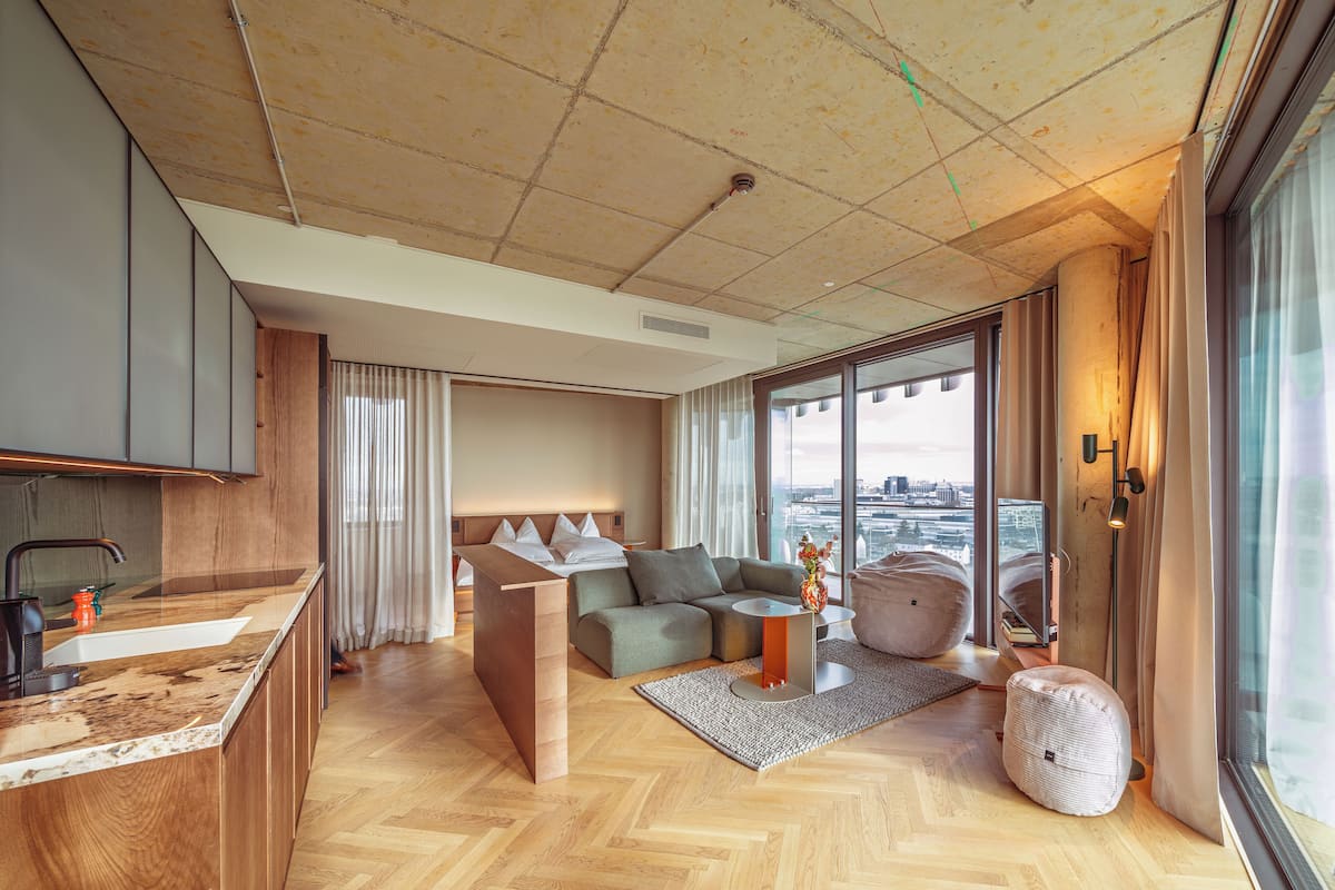 Una camera d'hotel moderna con pavimento in legno, un divano, un tavolo da pranzo e un'ampia finestra con vista sulla città.
