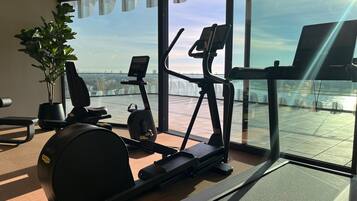 Un gimnasio con equipo de ejercicio, una planta en maceta y vistas a la ciudad a través de amplios ventanales.
