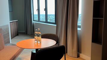 Une pièce moderne avec une table ronde, deux chaises, un canapé, une grande fenêtre avec des rideaux et une vue sur la ville.