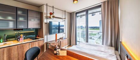 Ein modernes Hotelzimmer mit Schreibtisch aus Holz, einem Bett, einem Fernseher und einem großen Fenster mit Blick auf die Stadt.