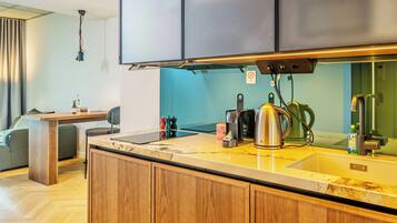 A modern kitchen with wooden cabinets, a stainless steel kettle, a coffee maker, and a small table with a chair.