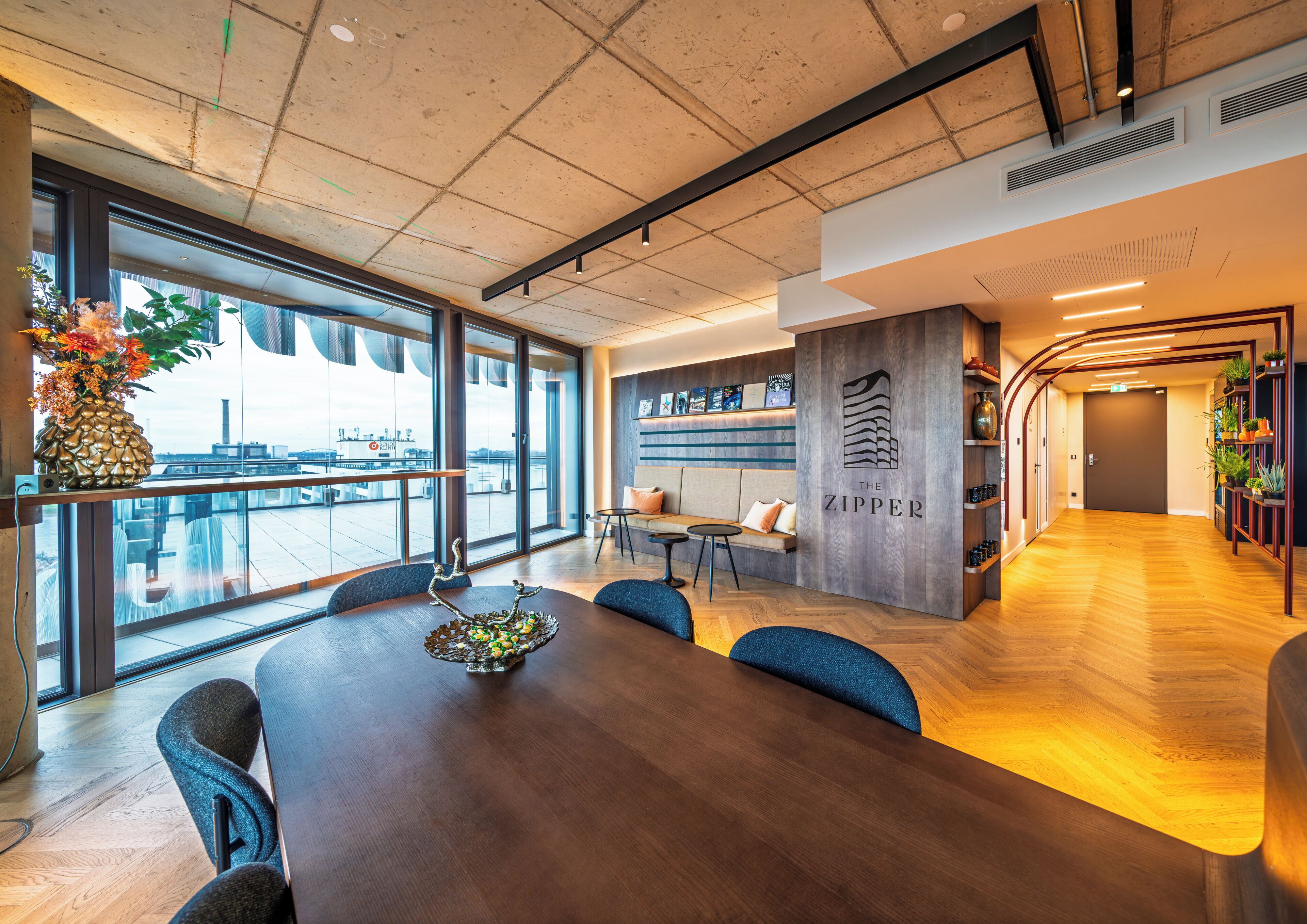 Eine moderne Hotelhalle mit einem Holzbüro, einer Sitzecke und Blick auf die Stadt durch große Fenster.