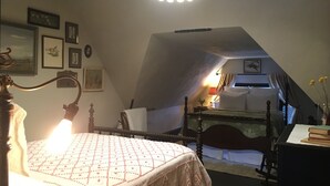 Un dormitorio con cama, escritorio y silla. Se observan cuadros enmarcados en la pared y un candelabro sobre la cama.
