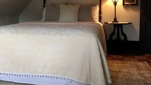 Un dormitorio acogedor en el ático con una cama grande, un espejo, una lámpara y una mesita.