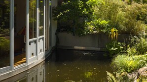 Una casa con balcón, estanque y abundante vegetación.