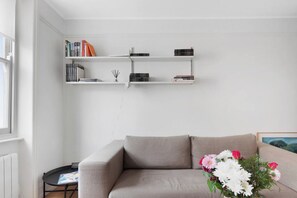 A living room with a grey sofa, a small round table, and a bookshelf with books and decorative items.