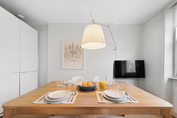 Un comedor con una mesa de madera preparada para dos personas, un frutero y vasos de jugo de naranja.