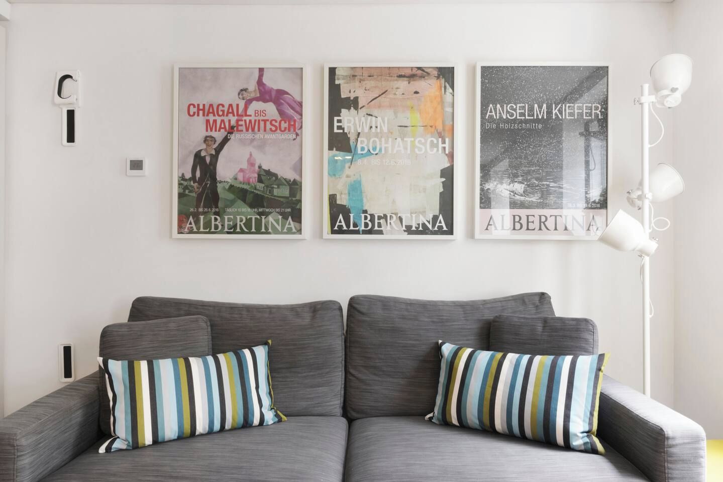 A modern living room with a grey sofa, striped pillows, and three framed artworks on the wall.