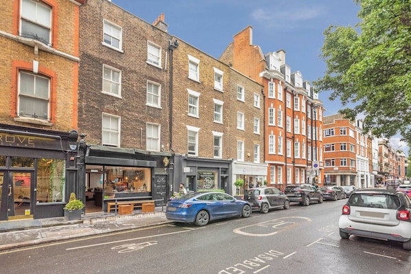 A street with parked cars, a bicycle lane, and buildings with shops.