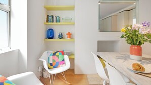 A modern kitchen with white and yellow shelves, a white chair, and a dining table with a plate of food.