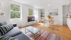 A modern living room with a sofa, a coffee table, and a TV. There is a dining area with a table and chairs.