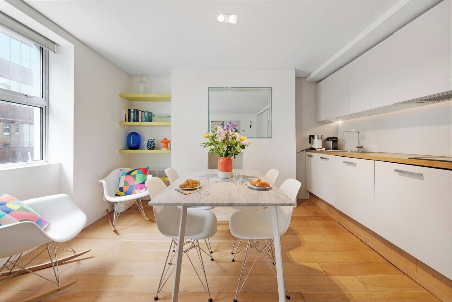 Een moderne keuken met witte kasten, een eettafel met stoelen en een raam met uitzicht.