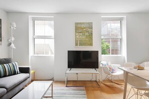 Una sala de estar moderna con un televisor de pantalla plana, un sofá, una mesa de comedor y dos ventanas.