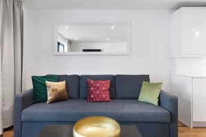 A modern living room with a grey sofa, a large mirror, and a wooden coffee table. - Hermitage Rd N4, Manor House | GroundFl | Garden (Greater London)