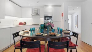 A modern kitchen with white cabinetry, a central island with a vase of flowers, and a dining table set for four. - Hermitage Rd N4, Manor House | GroundFl | Garden (Greater London)