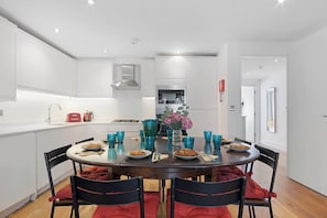 A modern kitchen with white cabinetry, a central island with a vase of flowers, and a dining table set for four.