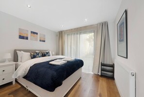 A modern bedroom with a large bed, bedside tables, a radiator, and artwork on the walls. - Hermitage Rd N4, Manor House | GroundFl | Garden (Greater London)