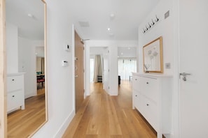 Un pasillo con piso de madera, paredes blancas y una puerta que da a un comedor.