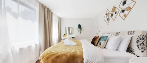 A modern bedroom with a large bed, bedside tables, a dresser, and a window with curtains.