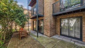 A modern building with a brick facade, a wooden table and chairs, and a covered outdoor area. - Hermitage Rd N4, Manor House | GroundFl | Garden (Greater London)